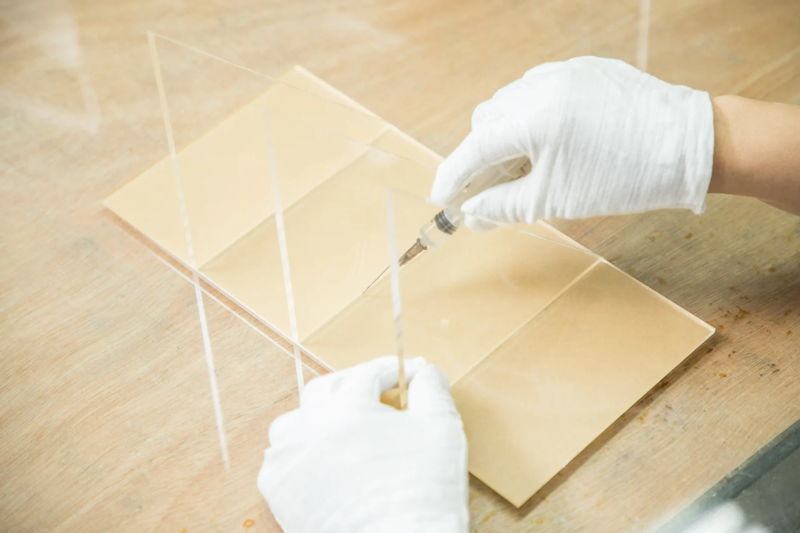 Gloved hands applying adhesive to a clear acrylic display assembly