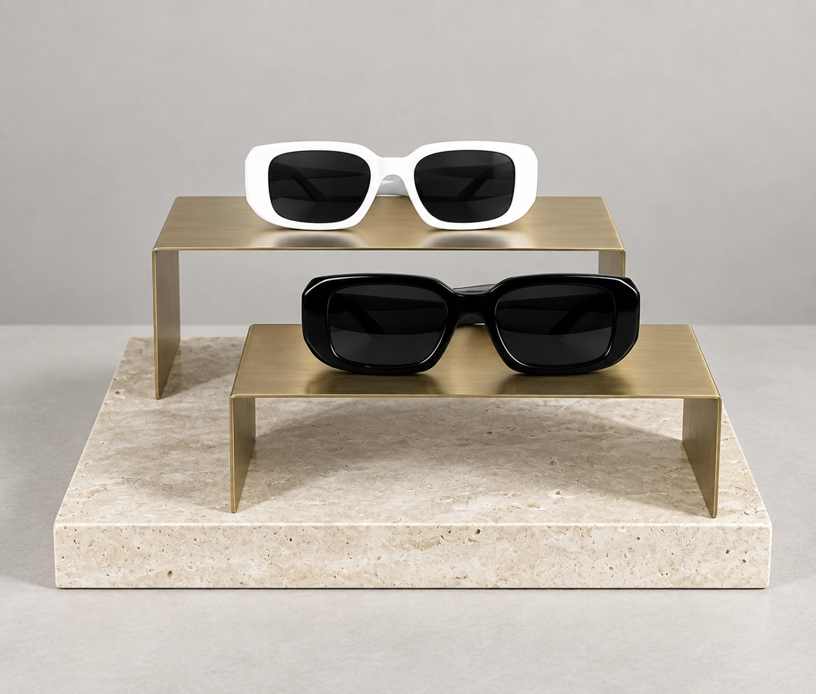 Black and white sunglasses on two brass-colored display risers