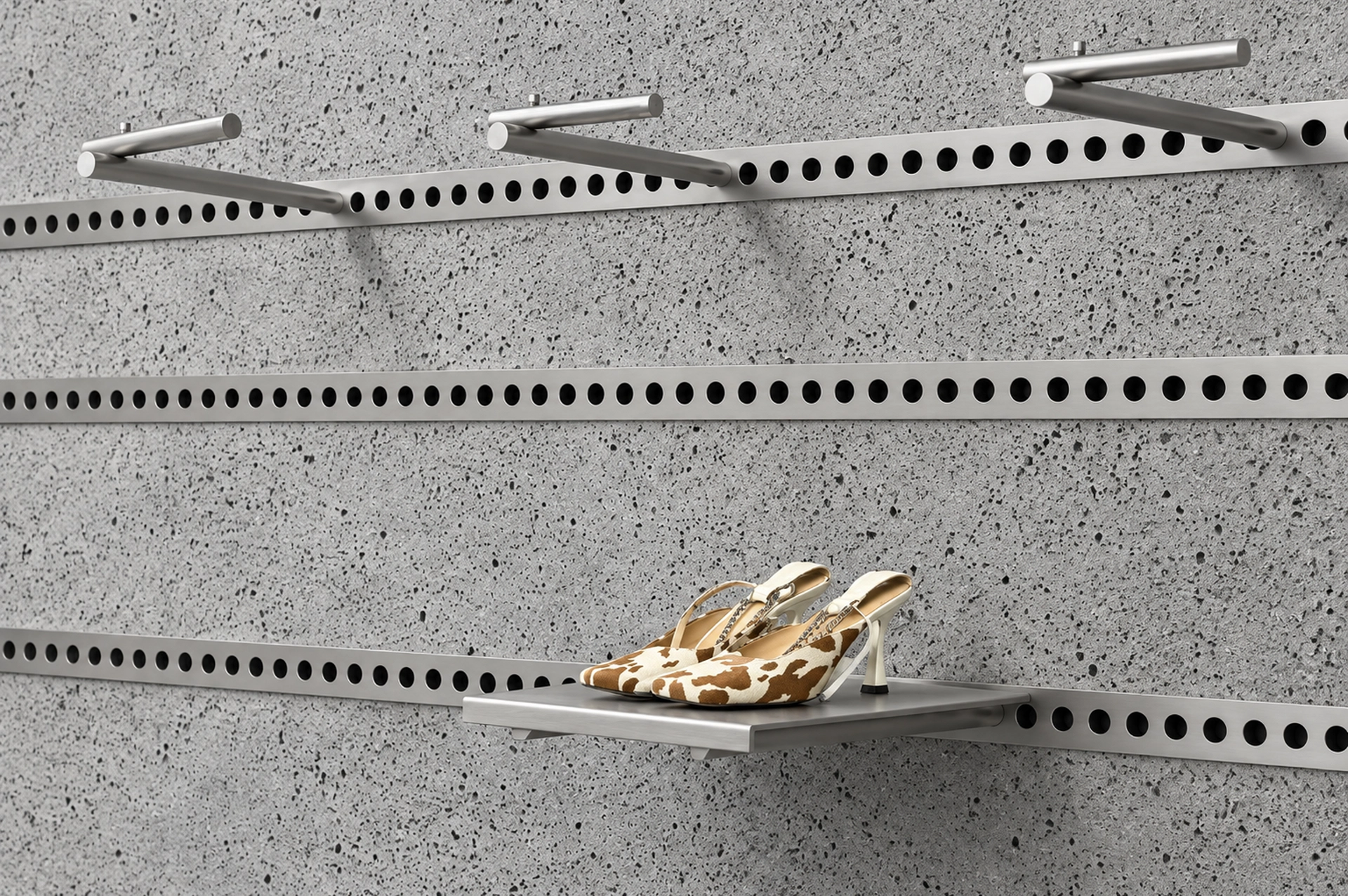 Modular wall display with perforated metal rails and a shoe shelf against a textured gray panel